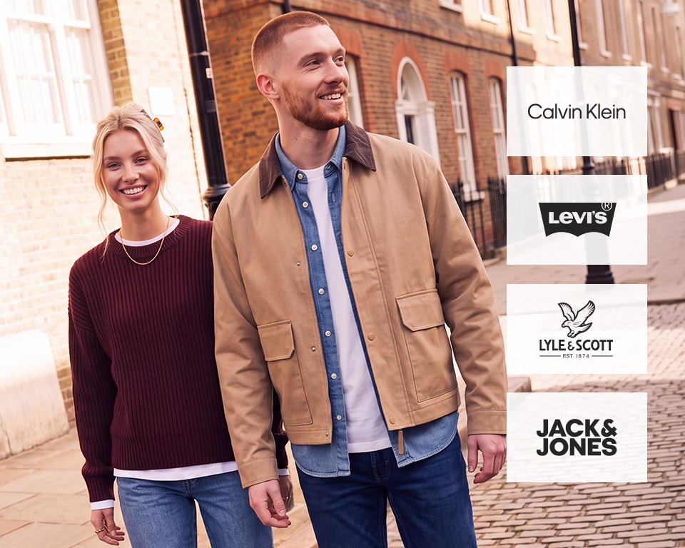 Smiling couple. Man in tan worker jacket, denim shirt, dark jeans. Woman in burgundy ribbed sweater, light jeans